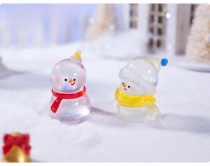 Macro shot of miniature glass snowmen with red and yellow scarves on snowy ground