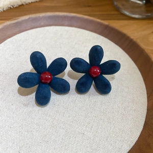 Close-up of deep blue flocked flower earrings with a red bead center on a wooden tray