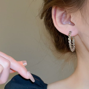 Close-up of a silver twisted chain texture hoop earring worn by a female model