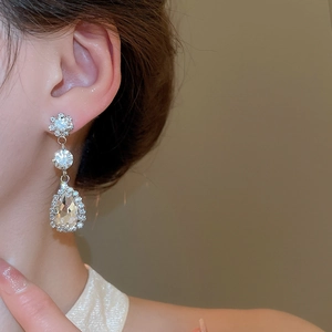 Detail of silver drop earrings with flower studs and pear-shaped crystals on model