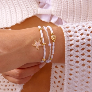 Close-up of bohemian layered bracelets with gold starfish, seashell charms and white beads