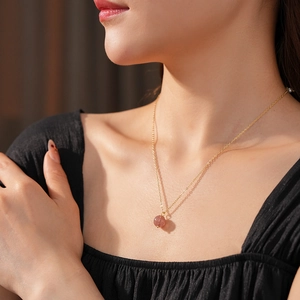 Detail of model wearing a gold necklace with a round pink stone pendant on her neck