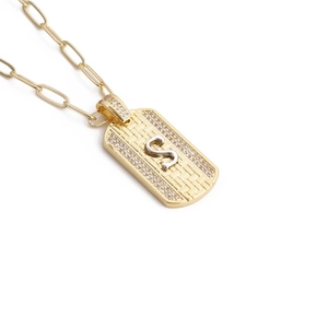 Détail macro du pendentif carré doré avec bordure en zircon et lettre S argent
