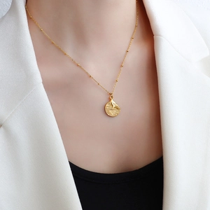 Golden titanium steel necklace with whale tail coin pendant worn on a white blazer