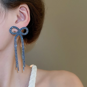 Close-up of model wearing blue rhinestone bow earrings with long tassel design