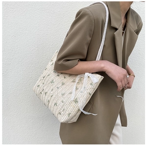 Detail of straw tote bag featuring green floral embroidery and white lace bow decoration