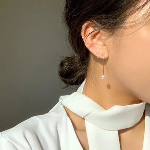 Detail view of gold long pearl drop earrings on model with warm sunset lighting