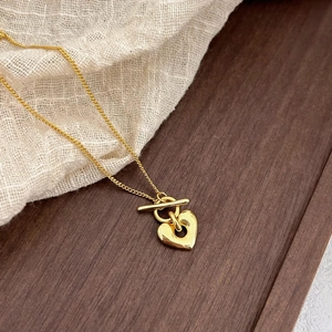 Detailed view of a gold heart pendant necklace with OT toggle clasp on a wooden tray