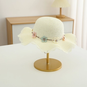 Détail du chapeau en paille crème avec chaîne florale et bordure ondulée élégante