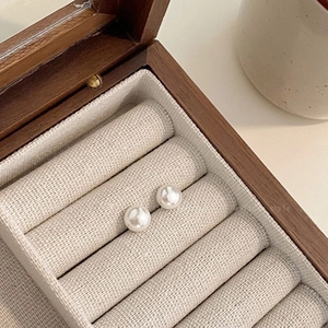 Close-up of minimalist white round pearl earrings on vintage wood and linen jewelry box display