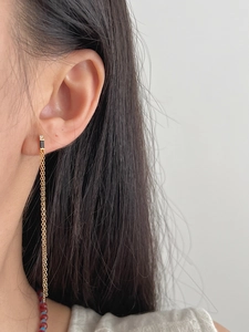 Detail of gold tassel earrings with black enamel rectangle and shimmering chain fringe