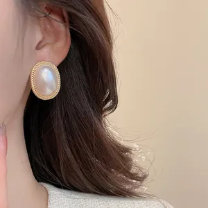 Close-up of vintage oval pearl earrings with golden twisted border on a female model