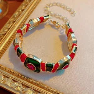 Macro detail of a vintage gold bracelet with green enamel and red beads on beige velvet