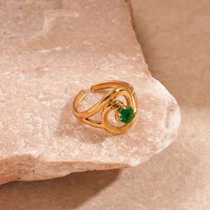 Detailed shot of a gold oval swirl ring with a green zircon on a pink stone background