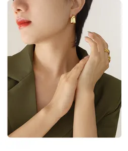 Détail de boucles d'oreilles dorées irrégulières en C et bague chaîne sur un mannequin