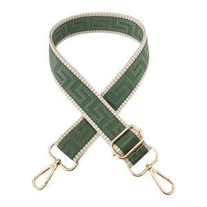 Detail of dark green woven bag strap with geometric labyrinth pattern and gold hardware
