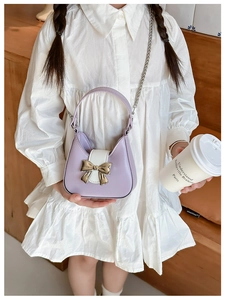 Detail of a purple and white PU leather kids handbag with a gold bow buckle on a model