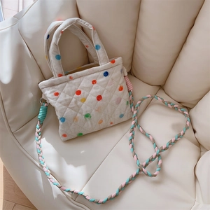 Detail of quilted polka dot mini bag featuring colorful woven shoulder strap and zipper