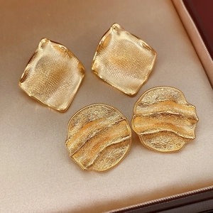 Gros plan détaillé de boucles d'oreilles dorées carrées et rondes sur du satin