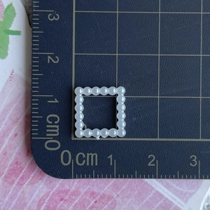 Macro shot of a small white pearl square frame charm measuring 1.5cm for DIY crafts