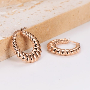 Polished rose gold croissant hoop earrings with spiral texture on stone surface