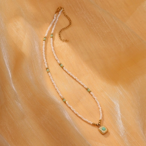 Detail of beaded necklace with white pearls, green beads and square golden pendant