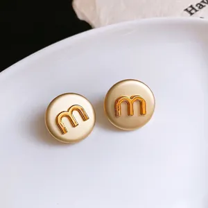 Minimalist gold round stud earrings with embossed letter M design on white plate