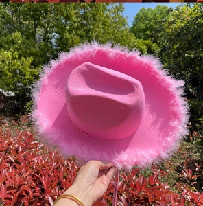 Detalle de sombrero de vaquero rosa con borde de plumas y una corona plateada frontal