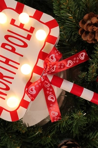 Close-up of LED Christmas North Pole sign with red bow against festive pine background