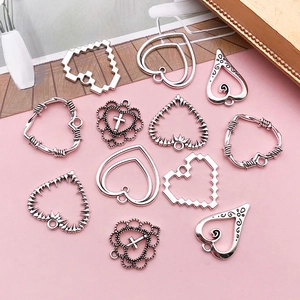 Flat lay of 12 vintage silver heart charms with hollow and tribal designs on pink surface