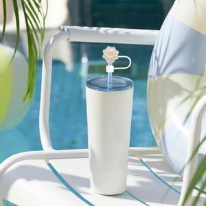 White tumbler with blue lid and decorative flower straw cover by a summer pool