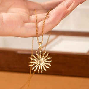 Detail of a gold sun pendant necklace held by hand over a wooden jewelry box