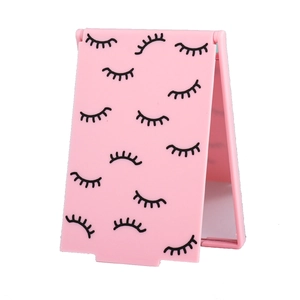 Pink foldable makeup mirror with eyelash pattern design standing on white background