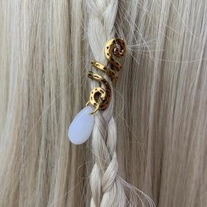 Detail of golden hammered spiral hair ring with white teardrop pendant on braided hair