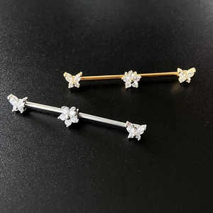 Macro detail of gold and silver industrial barbells with butterfly and floral crystal studs