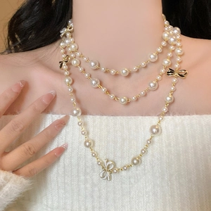 Close-up of a layered pearl necklace with gold chain and bow pendant on a model