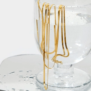 Elegant gold-plated triple layer flat snake chain necklace on a glass with bubbles