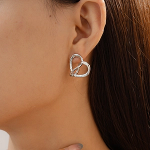 Macro shot of silver heart stud earrings with twisted hammer texture on model's ear
