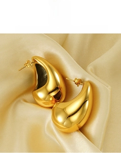 Close-up of polished gold teardrop earrings displayed on elegant champagne silk fabric