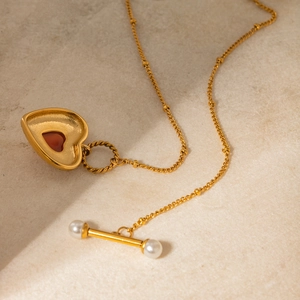 Detail of 18k gold heart necklace with red gemstone, pearl accent and T-bar toggle clasp