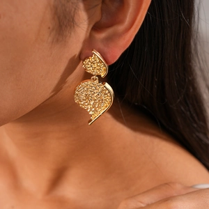Close-up of gold textured heart drop earrings worn to show the metallic pleated detail