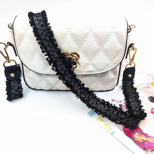 Close-up of quilted white PU leather bag with gold floral clasp and tassel strap