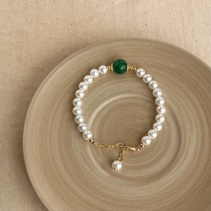 Baroque natural pearl bracelet with green bead accent on elegant beige ceramic tray