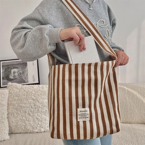 Dettaglio borsa tote in tela a righe con etichetta del marchio e tracolla abbinata