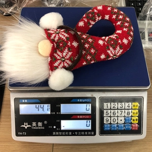 Vue détaillée d'un gnome de Noël en tricot rouge en cours de pesage sur une balance digitale