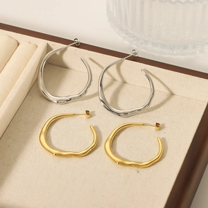 Irregular C-shaped stainless steel earrings in gold and silver on a beige display box