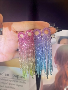 Detail of pink and blue gradient rhinestone tassel earrings held by hand for bridal wear