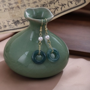 Detail of green jade ring earrings with white pearls and gold chains on a ceramic vase