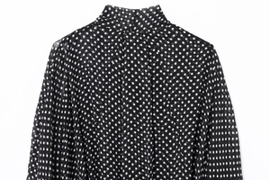Close-up of high neckline and pleated details on a black and white polka dot chiffon top