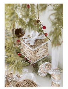 Detail of golden Christmas gift box ornament with white bow and pearls on a tree